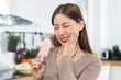 Face expression suffering from sensitive teeth and cold, asian young woman, girl hand touching her cheek, feeling hurt, pain eating ice cream, lolly. Toothache molar tooth at home, dental problem.
