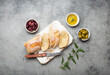 Sliced fresh ciabatta on cutting kitchen board, green and brown olives, olive oil with rosemary, olive tree branches on gray concrete stone rustic background from above copy space