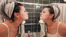 Woman Looking At Facial Mask In Front Of Bathroom Mirror At Night Routine