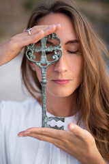 A girl on the seashore in a white dress holds an ancient key in her hands.