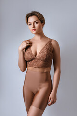 Poster - Portrait of young attractive woman wearing brown lace bra and high waist shaping briefs against gray background