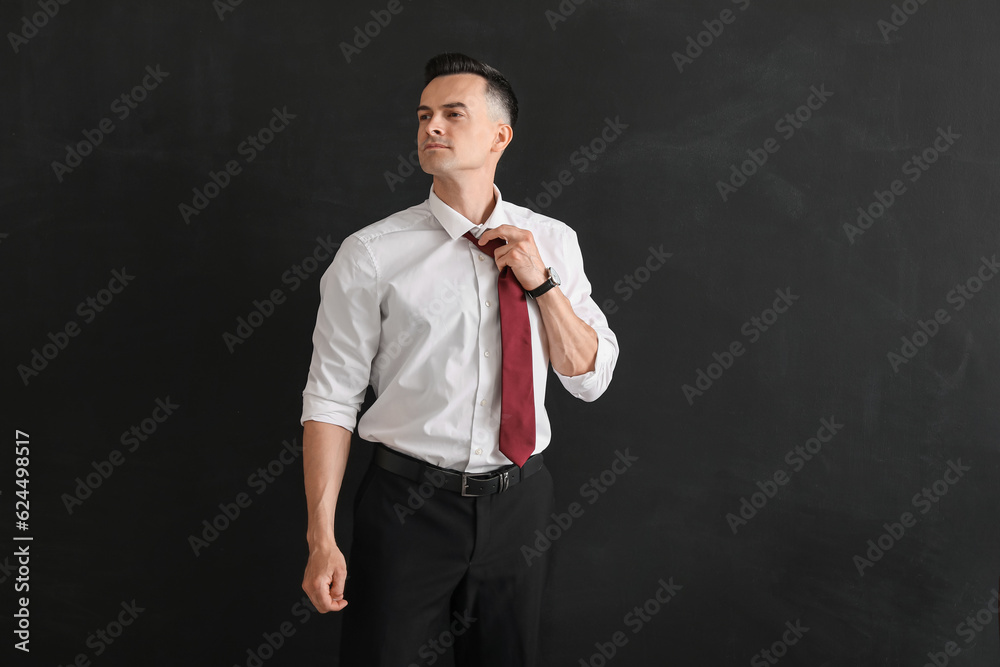 Male teacher fixing necktie near blackboard in classroom