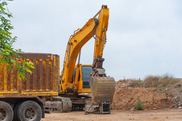 Wall Mural - Yellow excavator in a landfill with garbage and soil next to a truck ready for loading.