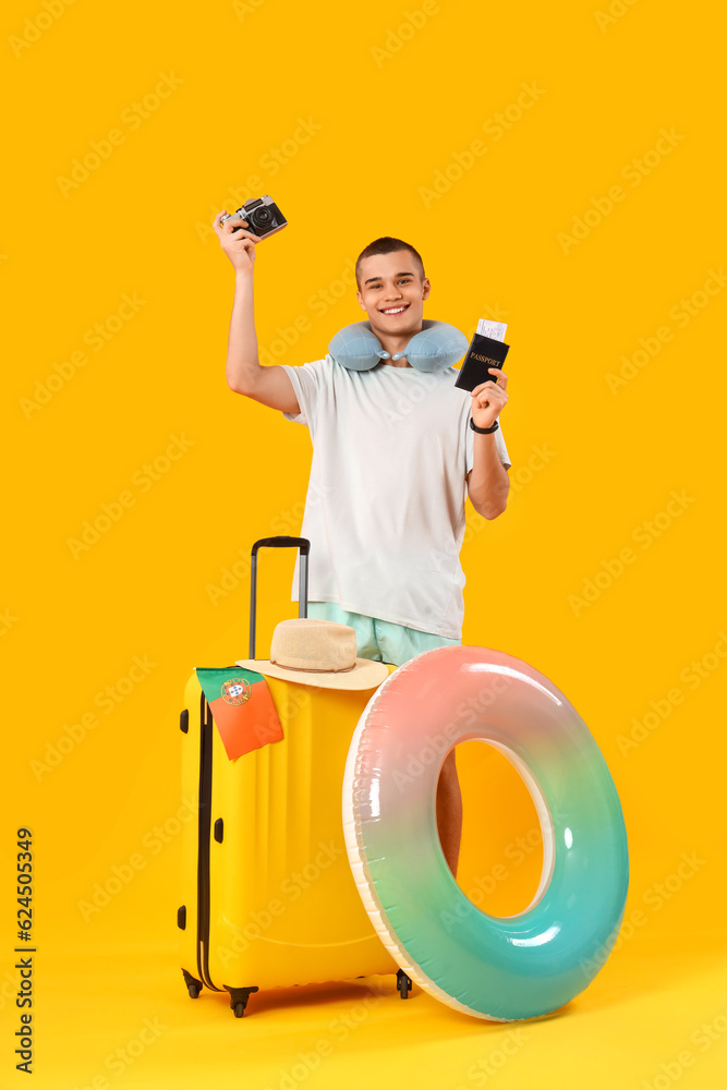 Teenage boy with beach accessories and suitcase on yellow background