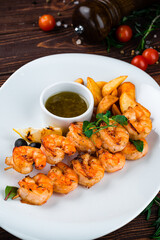 Wall Mural - Fried shrimp on a skewer with rustic potatoes, lemon, tomatoes, olives and sauce in a plate.