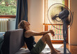 © olezzo - Young woman sitting at home on the floor in front of a fan saving from heat