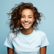 Portrait of a smiling young adult African woman with curly brown hair on a blue background. Happy young woman with a smile in a blue shirt with wavy hair. African American woman with shiny white teeth