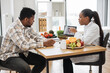 © sofiko14 - African american specialist in nutrition holding tablet with gastrointestinal tract on screen while counseling man at work. Focused woman explaining client about food intolerance during appointment.