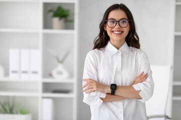 Smiling confident young european woman manager in glasses and white shirt with crossed arms