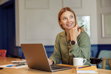 Wall Mural - Smiling woman entrepreneur working on laptop in modern coworking. Distance work concept