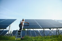 Man Engineer In Uniform Working On Solar Panels Power Farm. Solar Panel Field. Clean Energy Production. Green Energy.