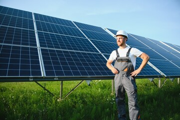 Wall Mural - Side view of male worker installing solar modules and support structures of photovoltaic solar array. Electrician wearing safety helmet while working with solar panel. Concept of sun energy