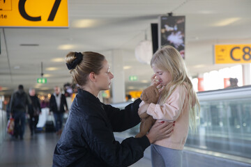 Wall Mural - Young woman comforting child lost at the airport who can't find her parents. Mother consoling upset little crying girl which got scared from flight at the airport.