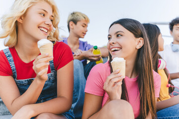 Group of happy friends, multiracial teenagers eating ice cream, talking  sitting on the street. Happy stylish boys and girls communication outdoors, having fun. Friendship, positive lifestyle, summer