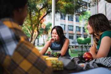 Wall Mural - Laughing student girls having a snack at the college campus while they are resting from studying