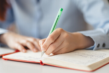 Closeup of female hand taking notes in notebook, selective focus. Student studying, learning language, examination, education concept  