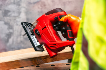 Wall Mural - Male worker holds a close-up jigsaw electric in his hands against the background of a concrete wall.