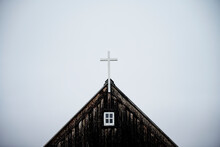 Weathered Wooden Church With Cross On Roof Against Overcast Sky