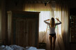 © Cavan Images - A young woman opens the curtains in the morning.