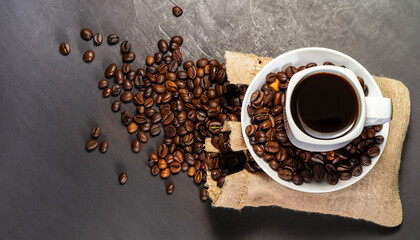 Wall Mural - cup of coffee and coffee beans in a sack on dark background, top view