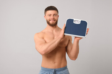 Poster - Happy athletic man holding scales on light grey background. Weight loss concept