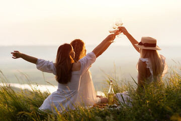 Lovely ladies drinking wine at sunset. Summer happy mood. Girlfriends relaxing on summer sunset with river on the background.	
