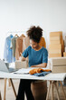 © Nuttapong punna - Young African woman running online store Startup small business SME, using smartphone or tablet taking receive and checking online purchase shopping order in office