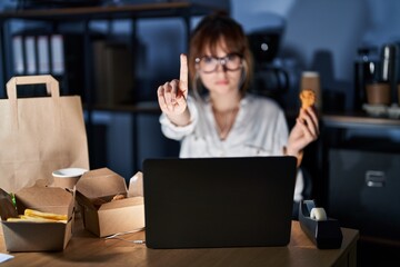 Canvas Print - Young beautiful woman working using computer laptop and eating delivery food pointing with finger up and angry expression, showing no gesture