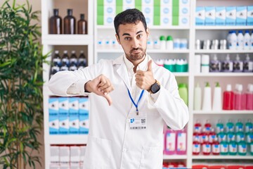 Sticker - Handsome hispanic man working at pharmacy drugstore doing thumbs up and down, disagreement and agreement expression. crazy conflict