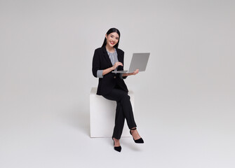 Young businesswoman asian happy smiling. While her using laptop sitting on white chair isolated on copy space white studio background.