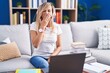 Young blonde woman studying using computer laptop at home bored yawning tired covering mouth with hand. restless and sleepiness.