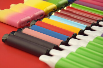 Wall Mural - Set of multicolor disposable electronic cigarettes on a red background.