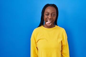 Wall Mural - Beautiful black woman standing over blue background sticking tongue out happy with funny expression. emotion concept.