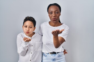 Wall Mural - Young mother and son standing together over white background looking at the camera blowing a kiss with hand on air being lovely and sexy. love expression.