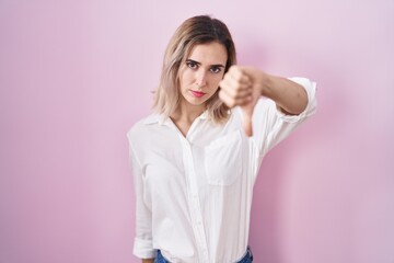 Canvas Print - Young beautiful woman standing over pink background looking unhappy and angry showing rejection and negative with thumbs down gesture. bad expression.