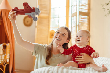 Wall Mural - Young happy babysitter playing airplane with cute little baby child