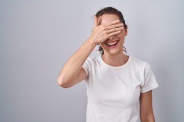 Sticker - Beautiful brunette woman standing over isolated background smiling and laughing with hand on face covering eyes for surprise. blind concept.