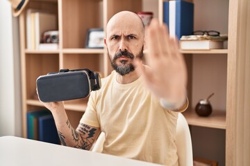 Canvas Print - Young hispanic man wearing virtual reality glasses with open hand doing stop sign with serious and confident expression, defense gesture