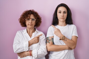 Poster - Hispanic mother and daughter wearing casual white t shirt over pink background pointing with hand finger to the side showing advertisement, serious and calm face