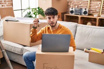 Sticker - Hispanic man with beard holding keys of new home doing video call with laptop scared and amazed with open mouth for surprise, disbelief face