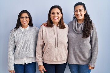 Wall Mural - Mother and two daughters standing over blue background with a happy and cool smile on face. lucky person.