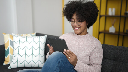 Poster - Young african american woman using touchpad sitting on sofa at home