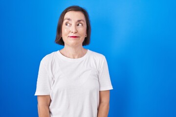 Poster - Middle age hispanic woman standing over blue background smiling looking to the side and staring away thinking.