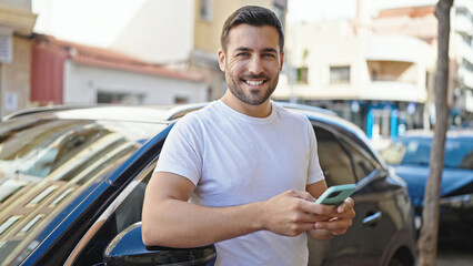 young hispanic man using smartphone leaning on car at street