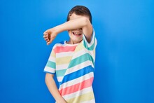 Young Caucasian Kid Standing Over Blue Background Covering Eyes With Arm Smiling Cheerful And Funny. Blind Concept.