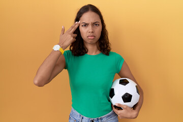 Poster - Young hispanic woman holding ball shooting and killing oneself pointing hand and fingers to head like gun, suicide gesture.