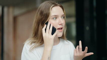 Poster - Young caucasian woman talking on smartphone with surprise expression at street