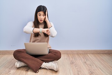 Poster - Young brunette woman working using computer laptop sitting on the floor looking at the watch time worried, afraid of getting late