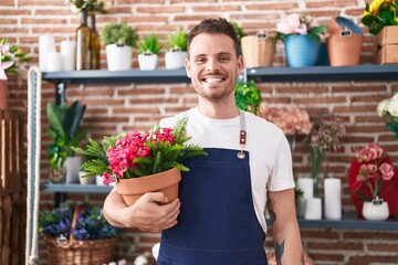 Poster - Young hispanic man working at florist shop holding plant pot looking positive and happy standing and smiling with a confident smile showing teeth