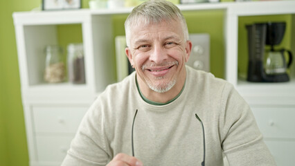 Poster - Middle age grey-haired man smiling confident sitting on table at home